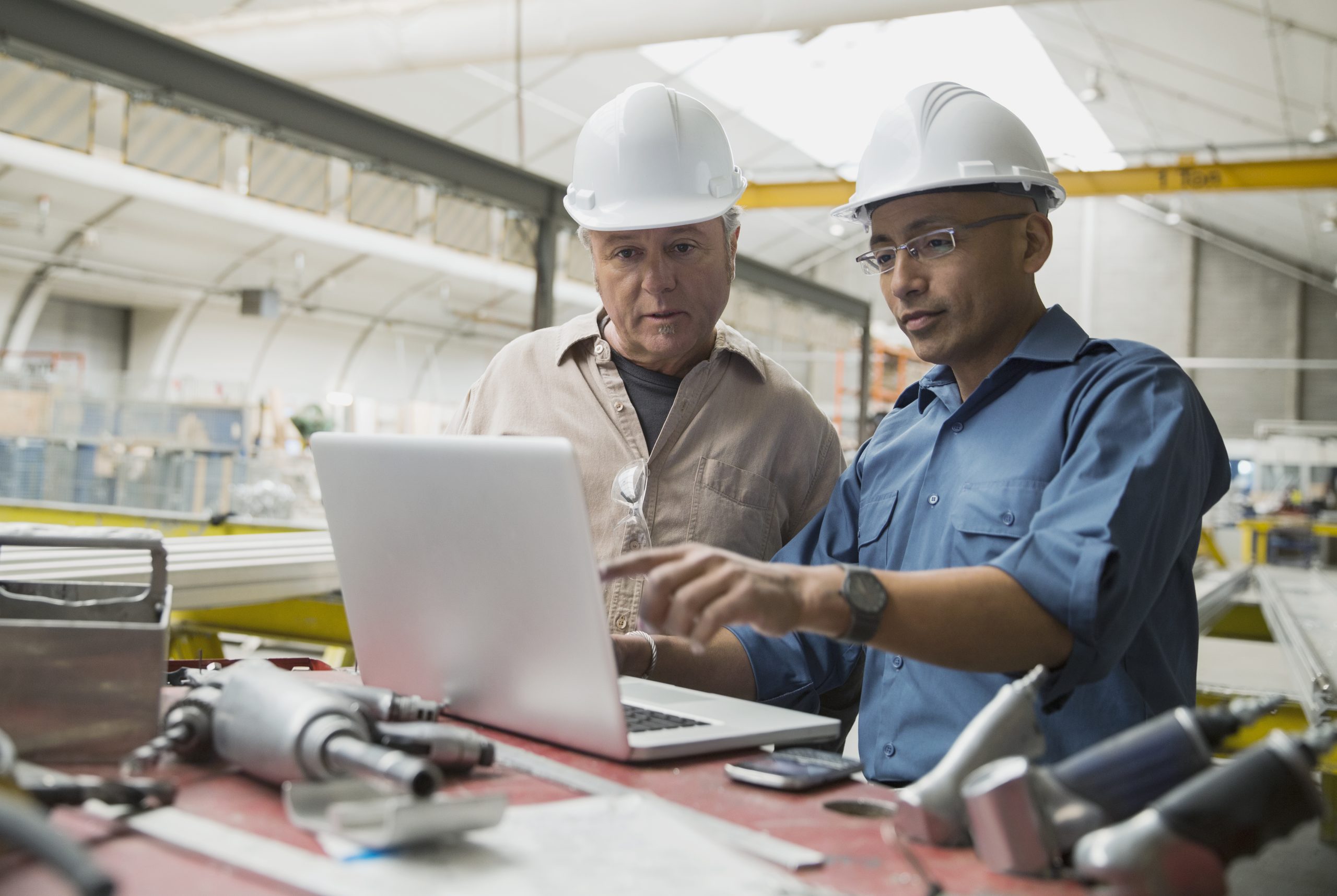 Depicts workers at laptop in a manufacturing plant